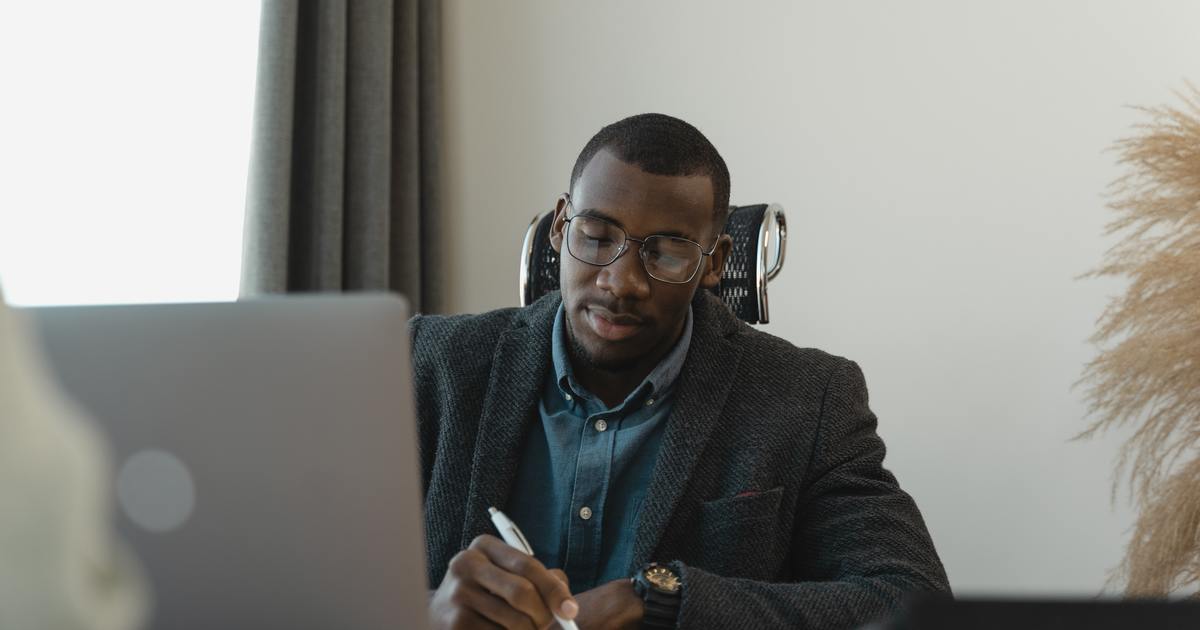 Writer taking notes on a piece of paper in front of a laptop