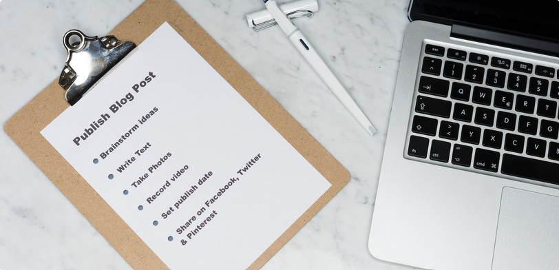 Photo of a clipboard next to a laptop on a desk. The clipboard contains a printed list for publishing a blog post. The list includes, Brainstorm ideas, write text, take photos, record video, set publish date, share on Facebook, Twitter, & Pintrest