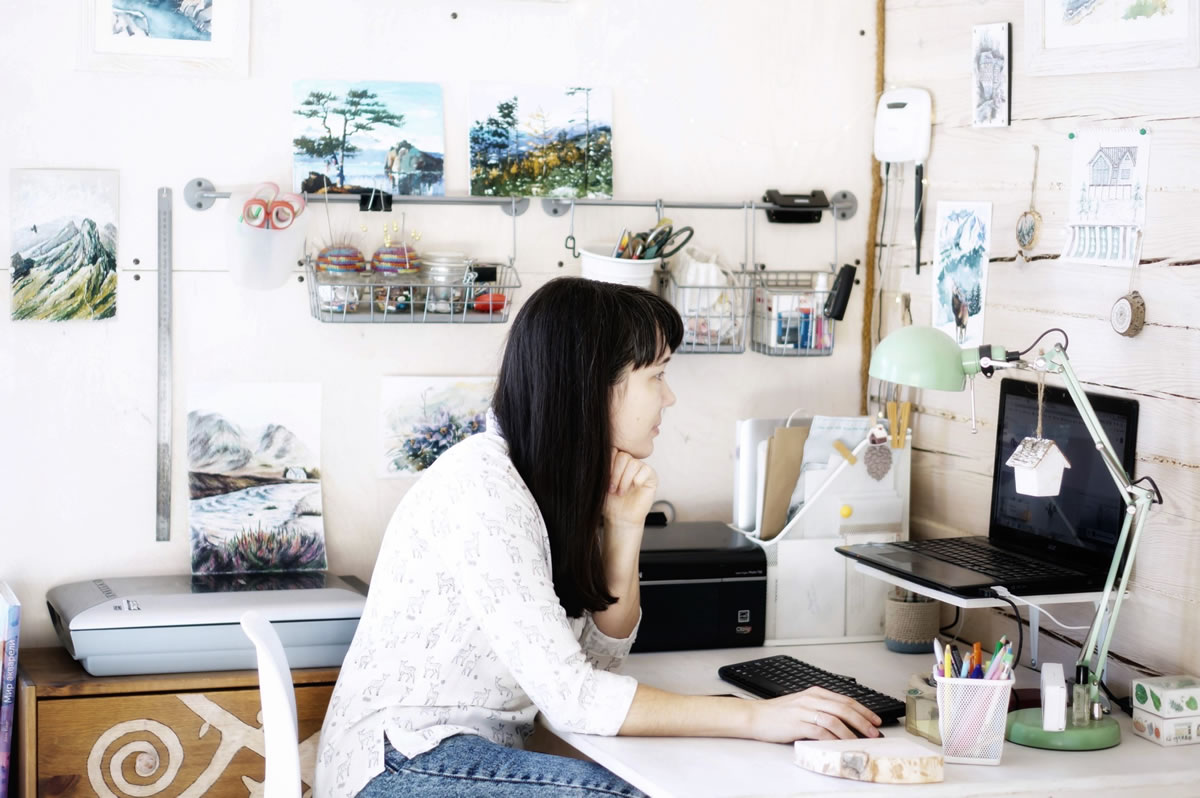 A woman sits at a desk using a computer in a creative, art-filled workspace.